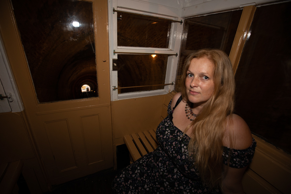 Emily Peasgood sits in the West Hill lift, in almost complete darkness. She is looking directly at the camera with no facial expression.