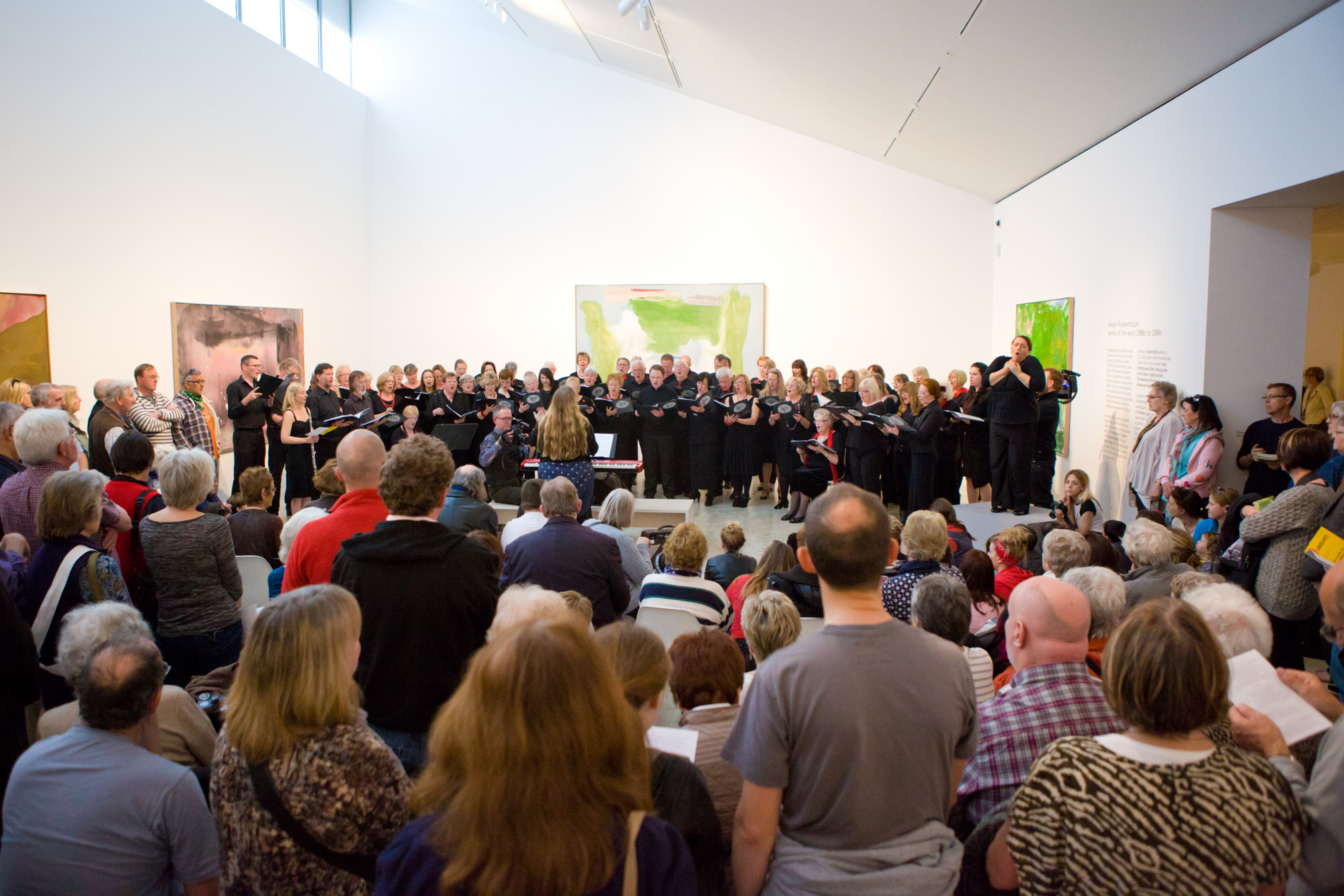The singers of Landscapes inside Turner Contemporary, performing at the premiere. They are standing in front of the paintings that inspired the work by JMW Turner and Helen Frankenthaler. A large audience surround them. 